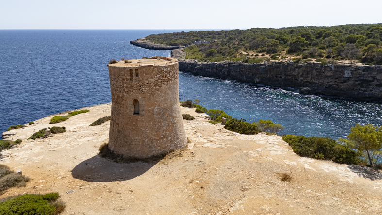 Historischer Steinturm an der felsigen Küste von Cala Pi mit Blick auf das Meer.