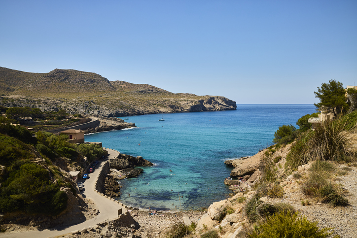 Weitwinkelblick auf Cala Sant Vicenç mit kleiner Badebucht, Küstenstraße und blauem Meer