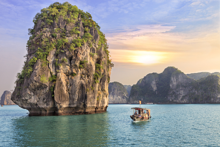 Ein kleines Boot fährt an einer markanten Felseninsel in der Halong-Bucht vorbei.