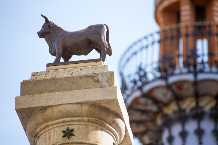 Kleine bronzene Stierfigur auf einer steinernen Säule vor unscharfem Hintergrund