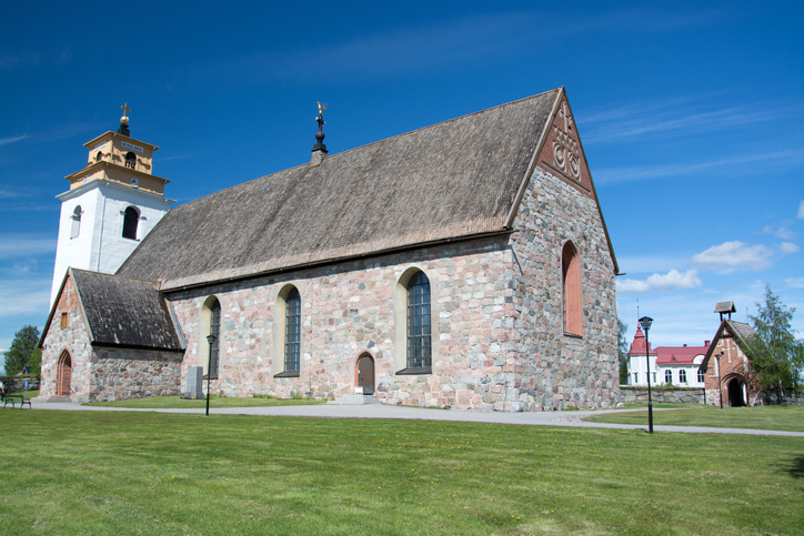 Historische Steinkirche mit hellem Turm und großem Kirchenschiff unter blauem Himmel bei Luleå.