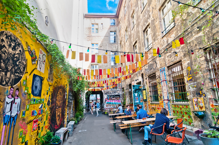 Ein bunter Innenhof mit Streetart, Lichterketten und Café-Tischen liegt in Berlin.