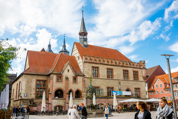 Das Alte Rathaus in Göttingen mit Fachwerk, Turm, Caféterrassen und Menschen auf dem Marktplatz.