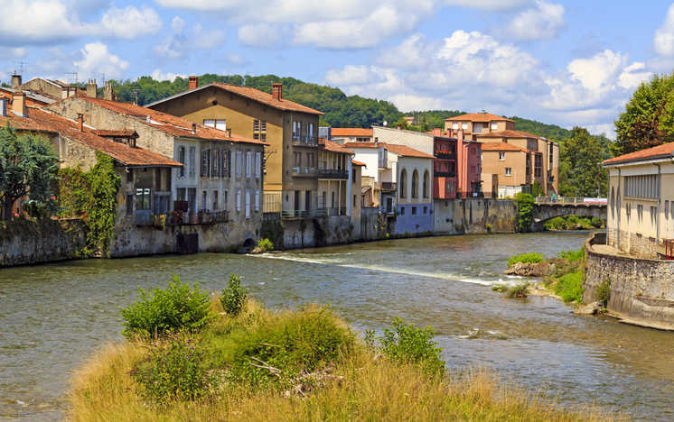Flusslauf mit Häusern, Ufergrün und kleiner Brücke im Stadtgebiet von Saint-Girons