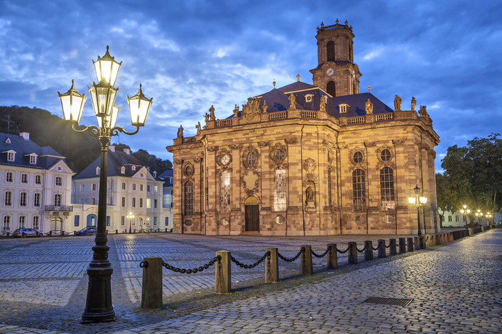 Die beleuchtete Ludwigskirche in Saarbrücken bei Abenddämmerung auf einem großen gepflasterten Platz.
