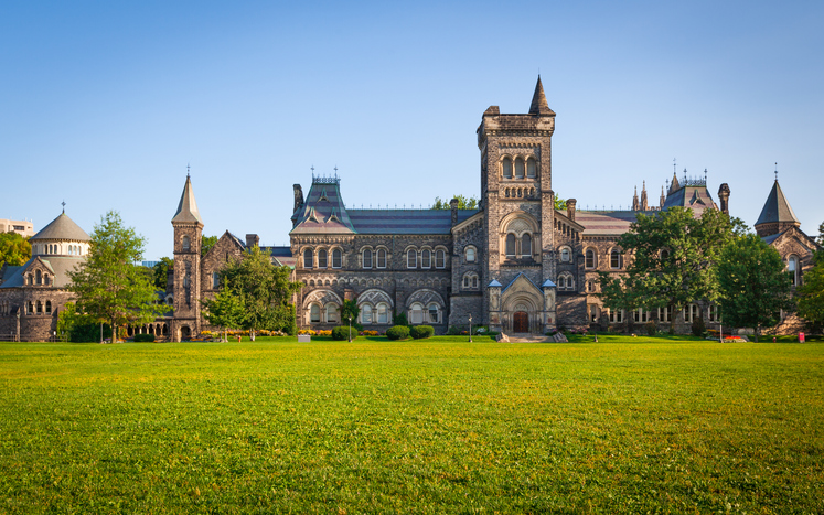 Großes historisches Universitätsgebäude in Toronto mit Türmen und weitläufiger Rasenfläche davor.
