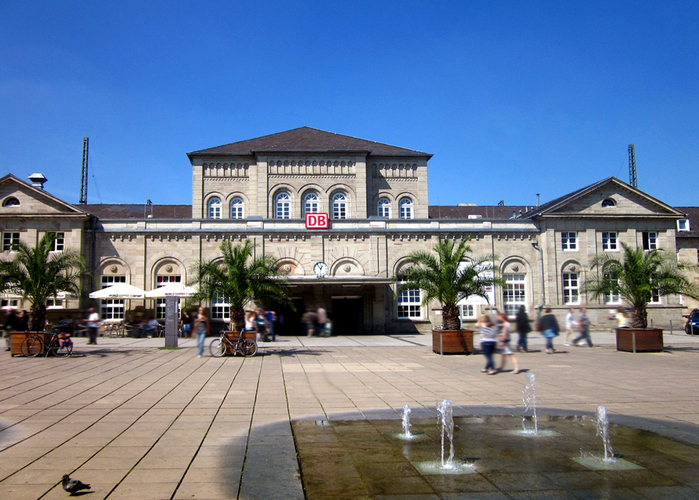 Der Hauptbahnhof Göttingen mit DB-Zeichen, Brunnen und Menschen auf dem Bahnhofsvorplatz.