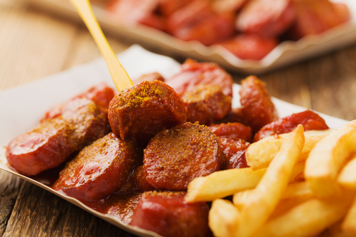 Currywurst mit roter Sauce, Currypulver und Pommes liegt auf einem Teller.