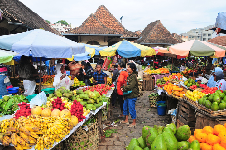 Ein belebter Markt in Antananarivo mit Obst, Gemüse und vielen Menschen unter bunten Sonnenschirmen.