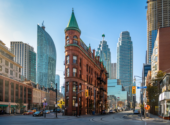 Schmal gebautes rotes Flatiron Building in Toronto mit Hochhäusern im Hintergrund.