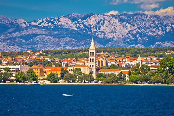 Blick auf Zadar am Meer mit Kirchturm, Altstadt und dem Velebit-Gebirge im Hintergrund.