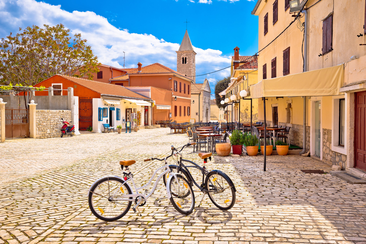 Fahrräder stehen auf einem hellen Steinplatz in der Altstadt von Zadar mit Kirchturm im Hintergrund.
