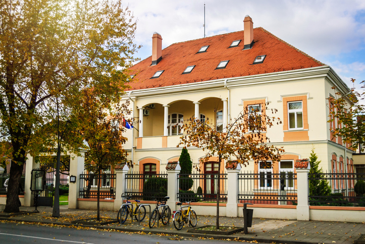 Elegantes helles Gebäude mit rotem Dach, Bäumen und Fahrrädern an einer Straße in Šabac