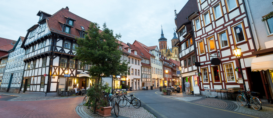 Eine Straße in Göttingen mit Fachwerkhäusern, Restaurants, Fahrrädern und beleuchteten Fenstern.