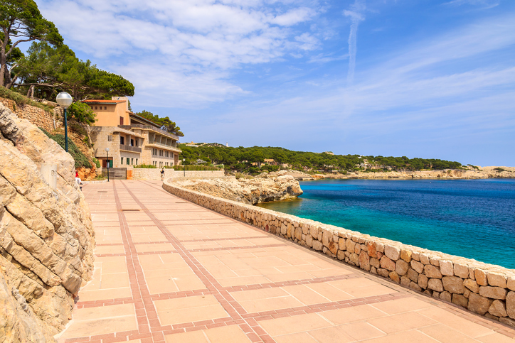 Uferpromenade mit Steinmauer und Blick auf das Meer bei Cala Gat