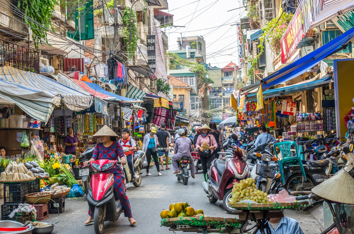 Eine belebte Straße in Hanoi mit Marktständen, Rollern, Fußgängern und vielen Stromleitungen.