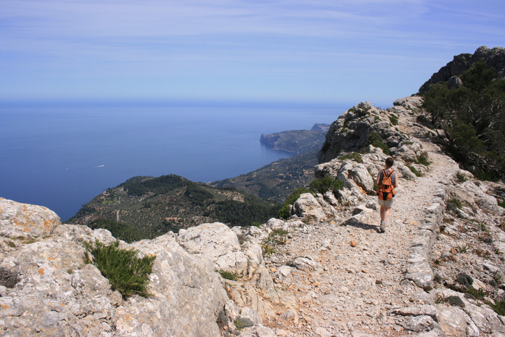 Wanderin auf einem felsigen Weg mit Blick auf die Küste im Tramuntana-Gebirge