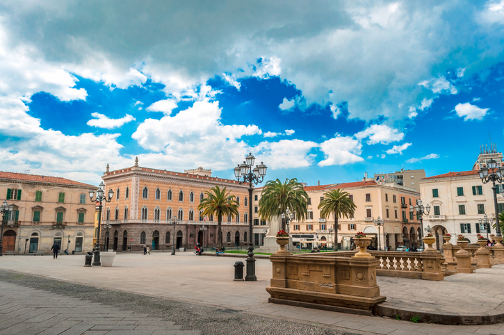 Weiter Platz mit Brunnen, Straßenlaternen und historischen Gebäuden unter wolkigem Himmel