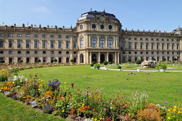 Die Würzburger Residenz mit großer Rasenfläche, Blumenbeeten und barocker Fassade.