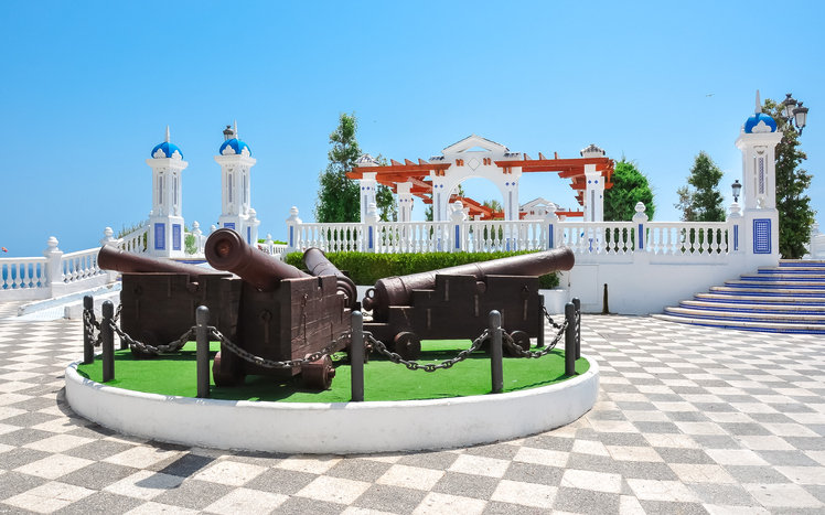Historische Kanonen auf einem gepflasterten Aussichtspunkt mit weiß-blauer Balustrade in Benidorm