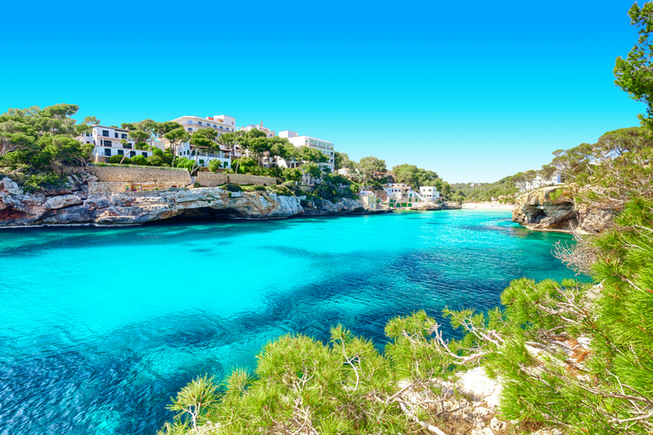 Weite Ansicht der Cala Santanyí mit türkisblauem Meer, Felsen, Pinien und weißen Häusern