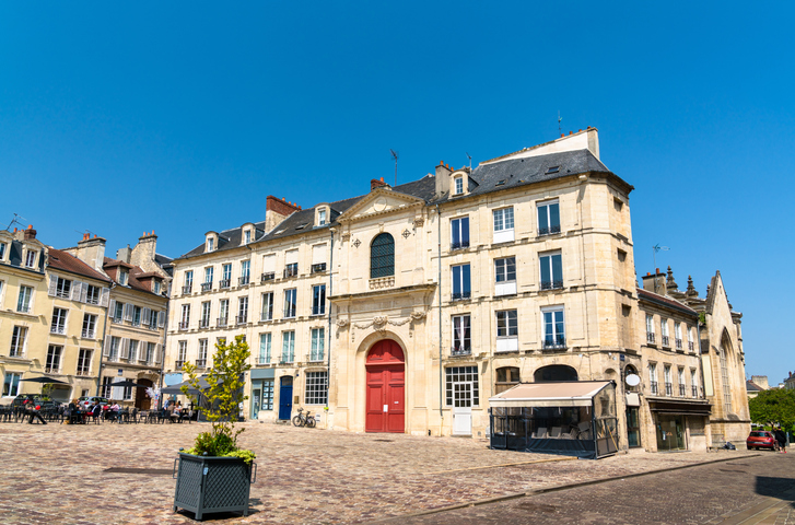 Historischer Platz in Caen mit hellen Natursteinfassaden, roten Türen, gepflastertem Boden und klassischer französischer Altstadtarchitektur.