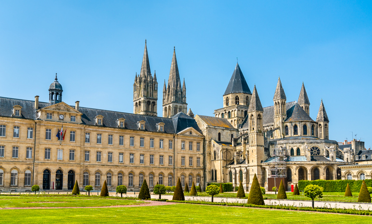 Große historische Kloster- und Kirchenanlage in Caen mit gepflegter Grünfläche, symmetrischen Gebäuden und markanten Türmen.