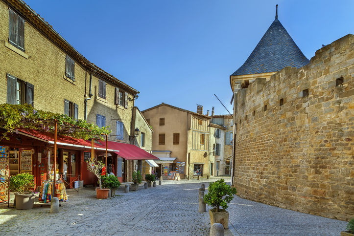 Eine gepflasterte Gasse in Carcassonne verläuft zwischen historischen Steinhäusern und einer massiven Stadtmauer mit Turm.