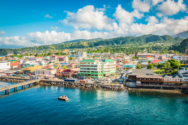 Panorama von Roseau auf Dominica mit türkisblauem Wasser, Uferpromenade, bunten Gebäuden und dicht bewachsenen Bergen im Hintergrund.