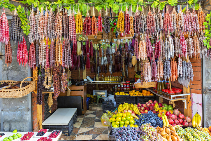 Marktstand in Tiflis mit bunten Churchkhela, frischem Obst, Flaschen und weiteren georgischen Spezialitäten.