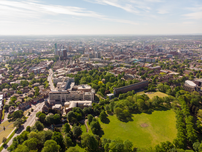 Weite Luftaufnahme von Leeds mit großflächigen Grünanlagen, dichter Stadtbebauung und moderner Skyline am Horizont.