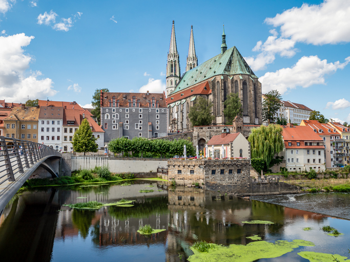 Große Kirche in Görlitz an der Neiße mit zwei schlanken Türmen, alter Steinfassade und Spiegelung im Fluss.