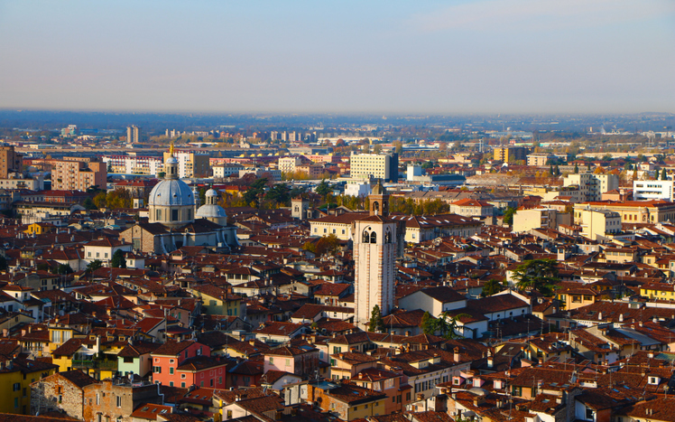 Blick über die Dächer von Modena mit dicht bebauter Altstadt, Kirchtürmen, Kuppeln und modernen Stadtvierteln am Horizont.
