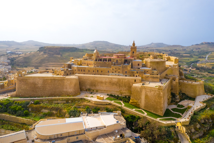 Luftaufnahme der befestigten Cittadella auf Gozo in Malta mit massiven Mauern, historischen Gebäuden und trockener Landschaft im Hintergrund.
