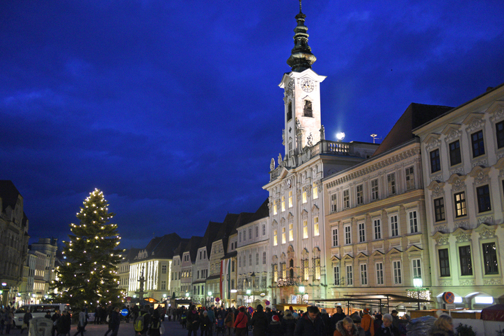 Belebter Stadtplatz in Steyr mit beleuchtetem Christbaum und historischem Rathaus am Abend.