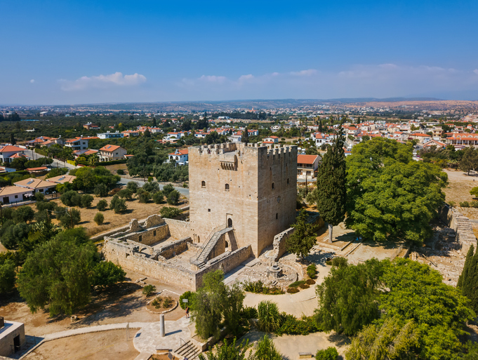 Kolossi Castle bei Limassol auf Zypern mit massivem mittelalterlichem Steinturm, umliegenden Ruinen und grüner Landschaft.
