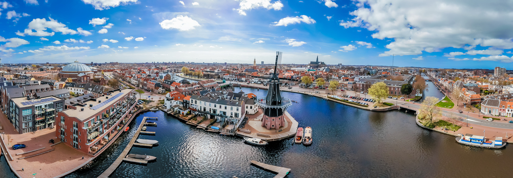 Luftaufnahme von Haarlem mit Windmühle De Adriaan, Grachten, historischen Häusern und weiter Stadtsilhouette unter wolkigem Himmel.