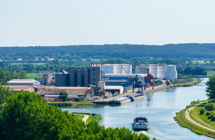 Industrie- und Hafenanlage am Main-Donau-Kanal in Erlangen mit großen Silos, Kränen, Frachtschiffen und grüner Landschaft.