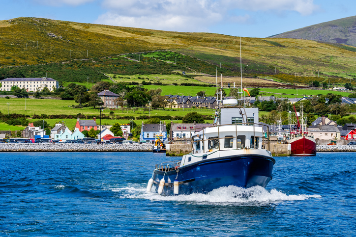 Kleines Boot auf blauem Wasser vor dem Hafen und grünen Hügeln bei Dingle