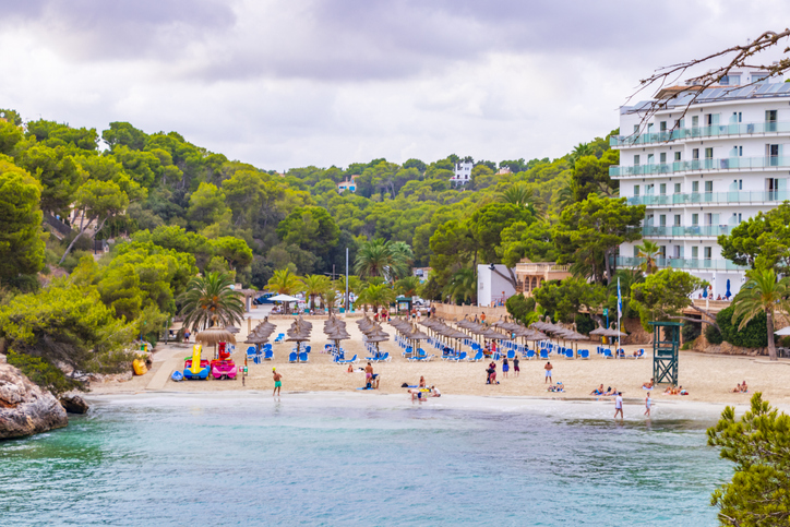 Strand von Cala Santanyí mit Liegen, Sonnenschirmen, Pinien und einem Hotel