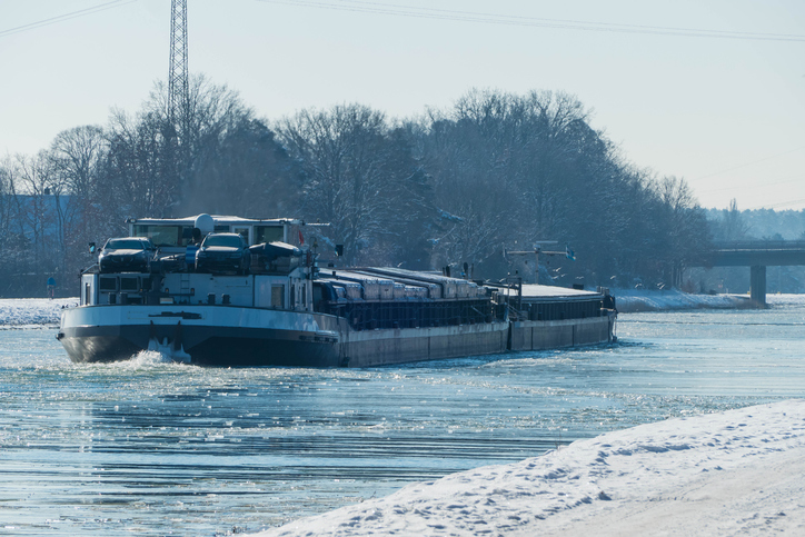 Großes Frachtschiff auf dem teilweise vereisten Main-Donau-Kanal bei Erlangen mit verschneiten Ufern und winterlicher Landschaft.
