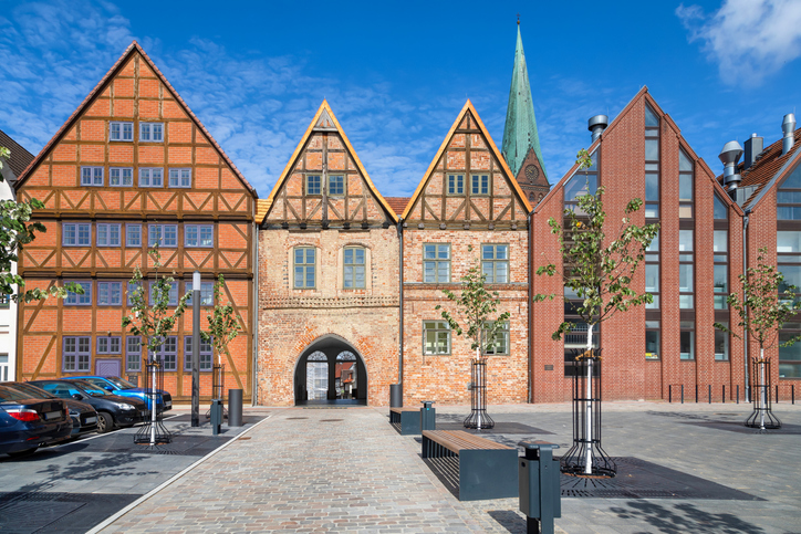 Fachwerkhäuser und Backsteinfassaden stehen an einem Platz in Schwerin, dahinter ragt ein hoher Kirchturm auf.