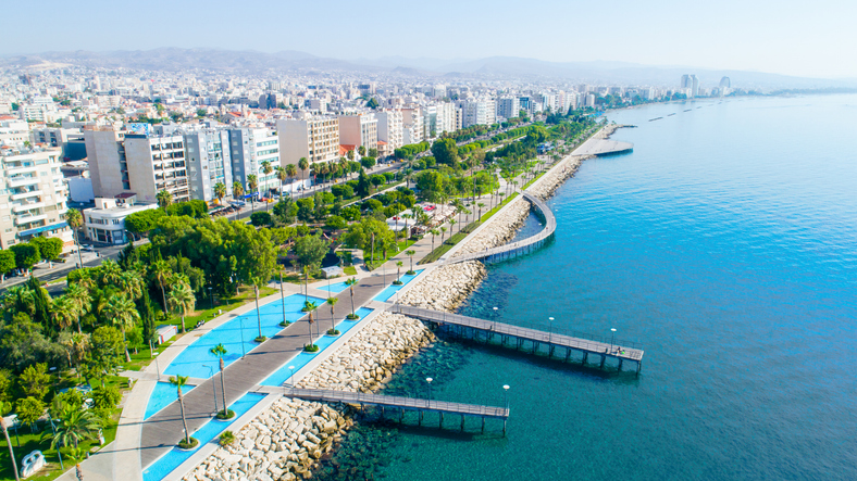 Luftaufnahme der Küstenpromenade von Limassol mit Grünanlagen, Palmen, modernen Gebäuden und ruhigem Mittelmeer.