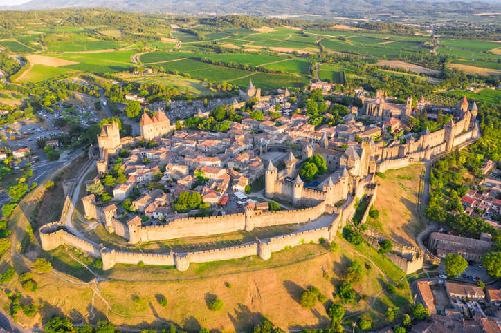 Ein Luftbild zeigt die vollständig ummauerte Altstadt von Carcassonne mit Türmen, Gassen und umliegender Landschaft.