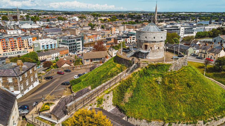 Luftaufnahme von Drogheda mit dem runden Turm von Millmount auf einem begrünten Hügel und dem Stadtzentrum im Hintergrund.