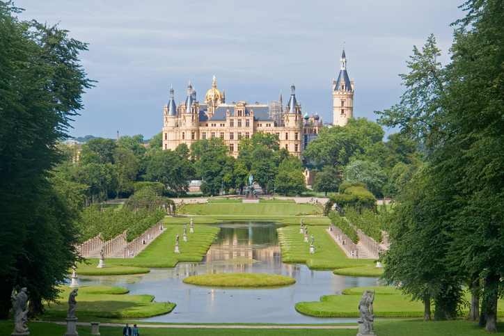 Eine symmetrische Gartenanlage mit Wasserbecken und Skulpturen führt den Blick auf das Schweriner Schloss.