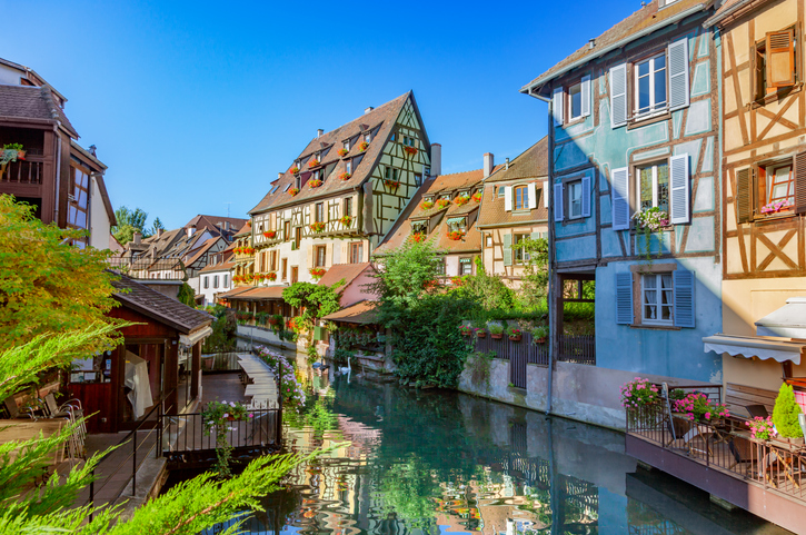 Ein Kanal führt durch ein Fachwerkviertel in Colmar, dessen Häuser mit Lichtern, Blumen und farbigen Fassaden geschmückt sind.