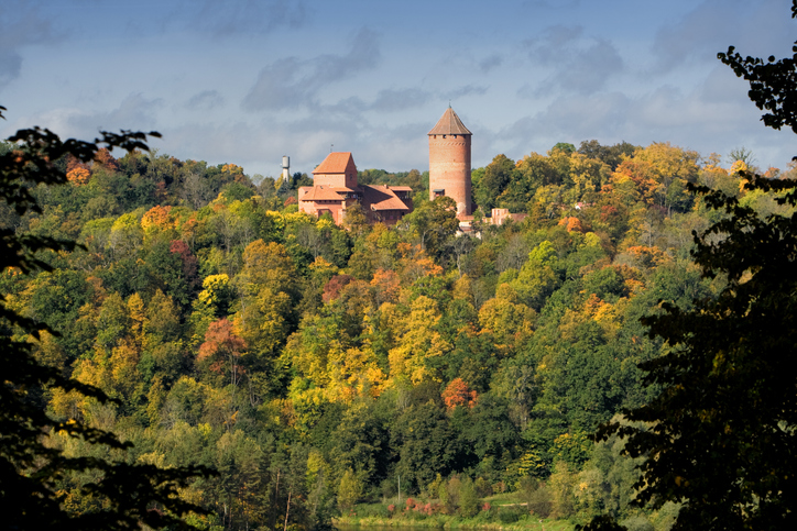 Schloss Turaida bei Sigulda in Lettland mit rotem Backsteinturm und historischen Gebäuden über einem herbstlich gefärbten Wald.