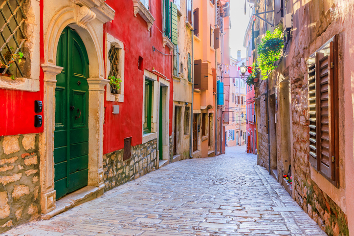 Schmale gepflasterte Altstadtgasse in Rovinj mit bunten Fassaden und grünen Fensterläden