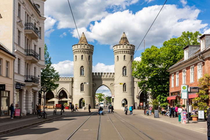 Nauener Tor in Potsdam mit zwei runden Türmen, spitzen Dächern, großem Torbogen und Straßenbahngleisen im Vordergrund.